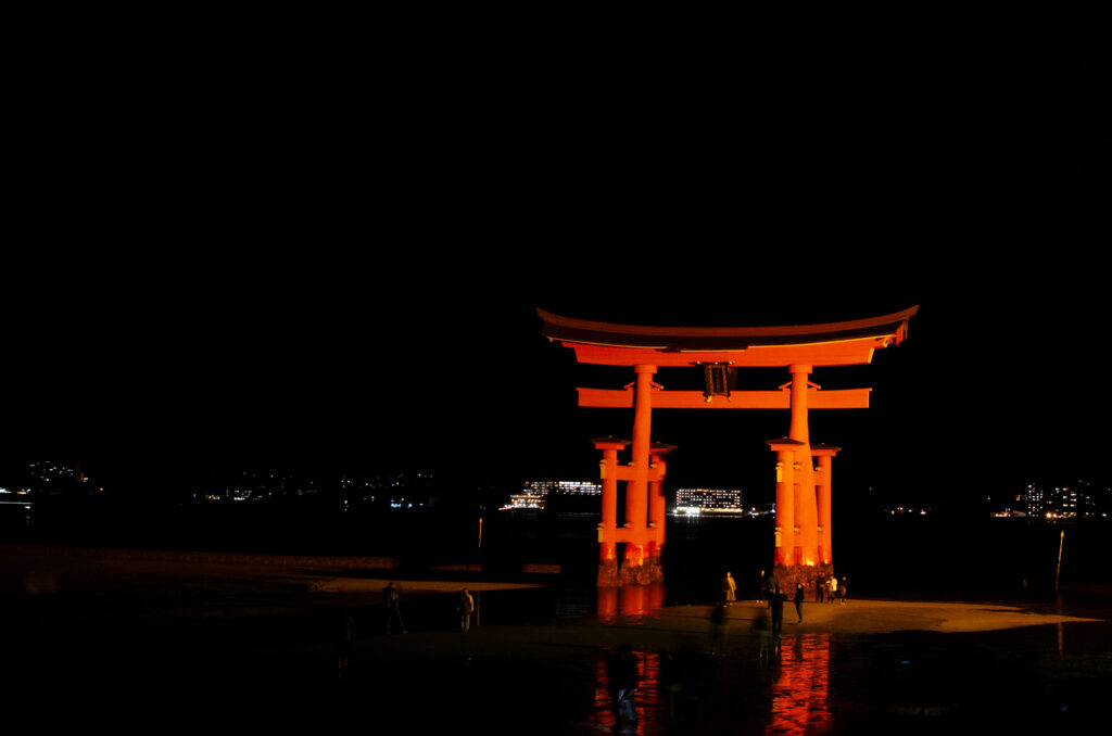 Illuminated torii gate at Miyajima at night reflecting on wet sand